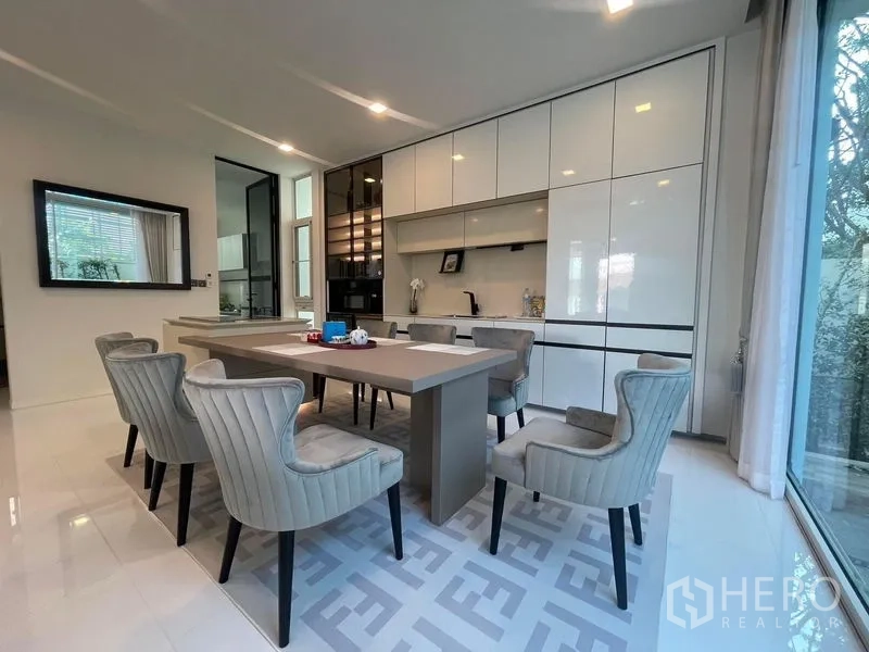 Detached House for rent in Bueng Kum, Bangkok - Dining area beside the kitchen with six upholstered chairs, oversized windows and white cabinets.