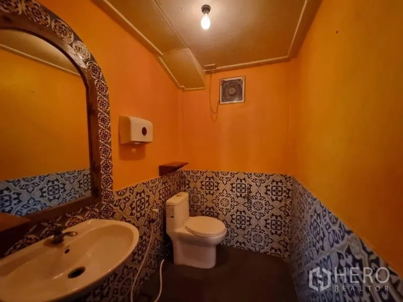 Detached House for rent in Khlong Toei, Bangkok - Bathroom with orange walls, patterned half-height tiles, sink and toilet.