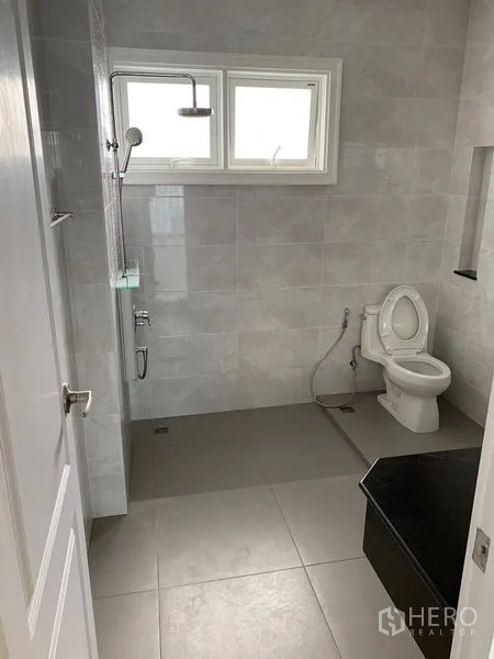 ทาวน์เฮาส์ ให้เช่าในBang Na, Bangkok - ห้องน้ำสมัยใหม่ มีเรนชาวเวอร์ โถสุขภัณฑ์ และกระเบื้องโทนเทาใต้หน้าต่าง