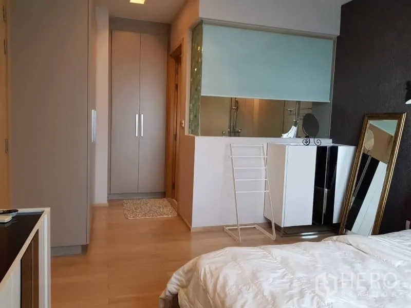 Condominium for rent in Khlong Toei, Bangkok - Bedroom with built-in wardrobes, vanity cabinet, and a glass partition to the bathroom.