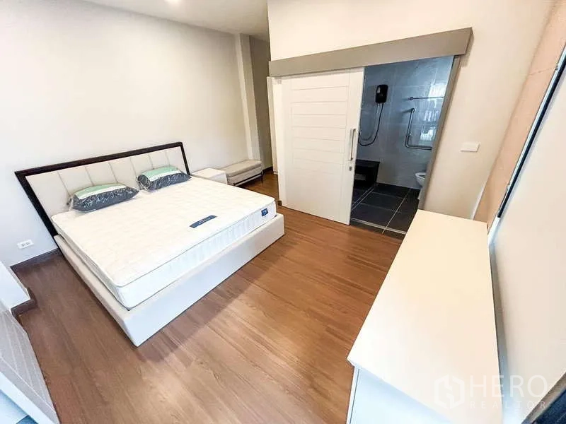 Detached House for rent in Bang Phli, Samut Prakan - Bedroom with wooden flooring and ensuite bathroom accessed via a sliding door.