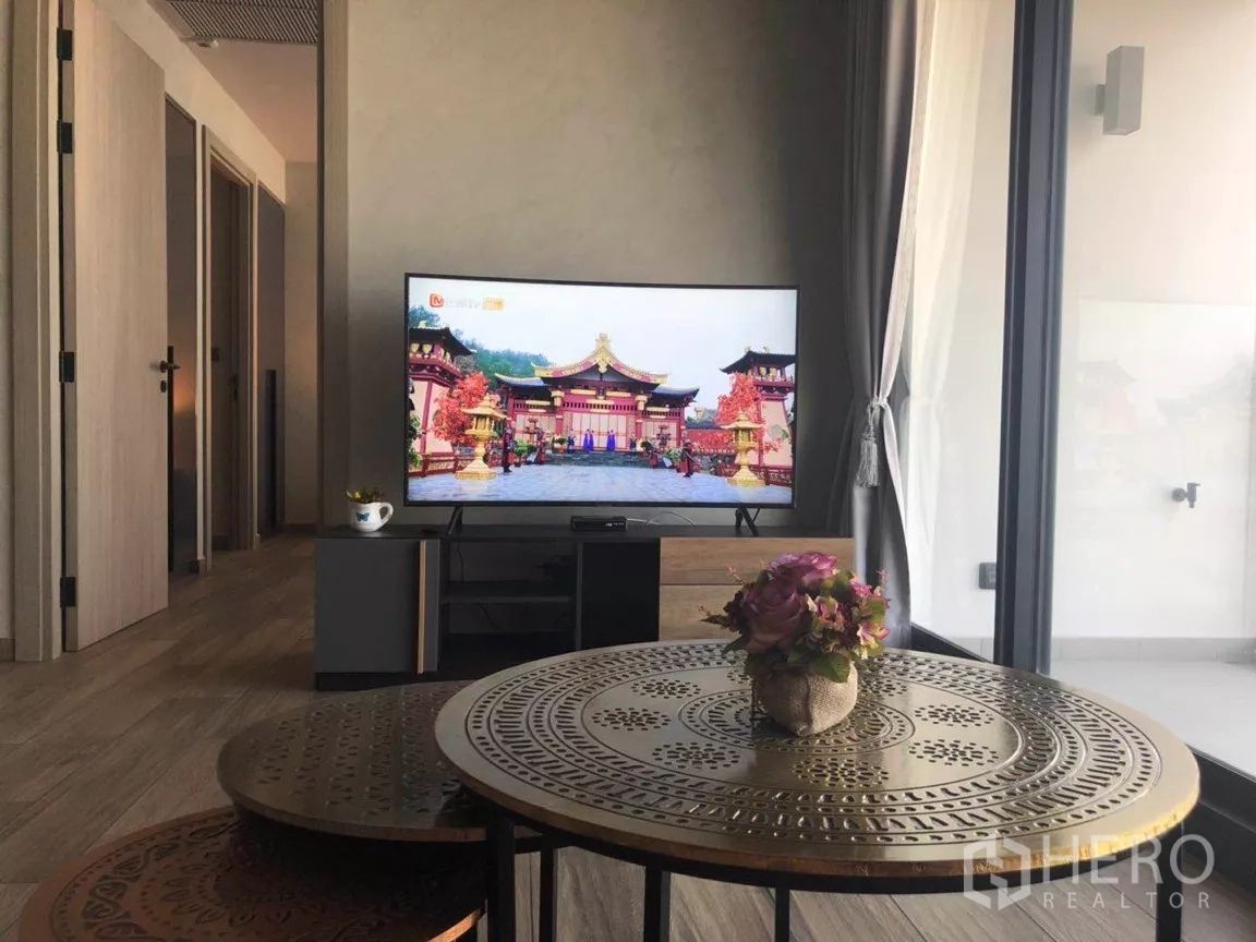 คอนโด ขายในWatthana, Bangkok - มุมทีวีจอแบนขนาดใหญ่บนตู้วางทีวี โต๊ะกลางโลหะทรงกลมพร้อมแจกันดอกไม้ และประตูกระจกสไลด์ออกระเบียง