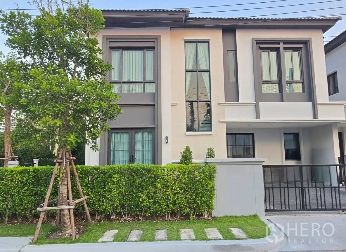 Detached House for rent or sale in Bang Phli, Samut Prakan - Modern two-storey house exterior with tall windows, trimmed hedge, and gated parking.