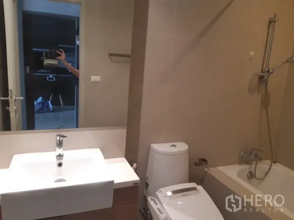 Condominium for rent in Bangkok - Bathroom with bathtub and handheld shower next to vanity and toilet.