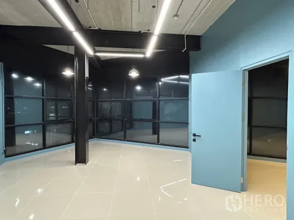 办公空间 出租在Chatuchak, Bangkok - 转角工作区，落地网格窗、黑色钢柱、蓝色墙面与开放式天花。