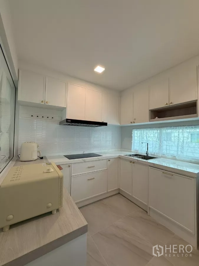 Detached House for rent in Bang Phli, Samut Prakan - Modern white L-shaped kitchen with induction cooktop, hood and ample cabinetry