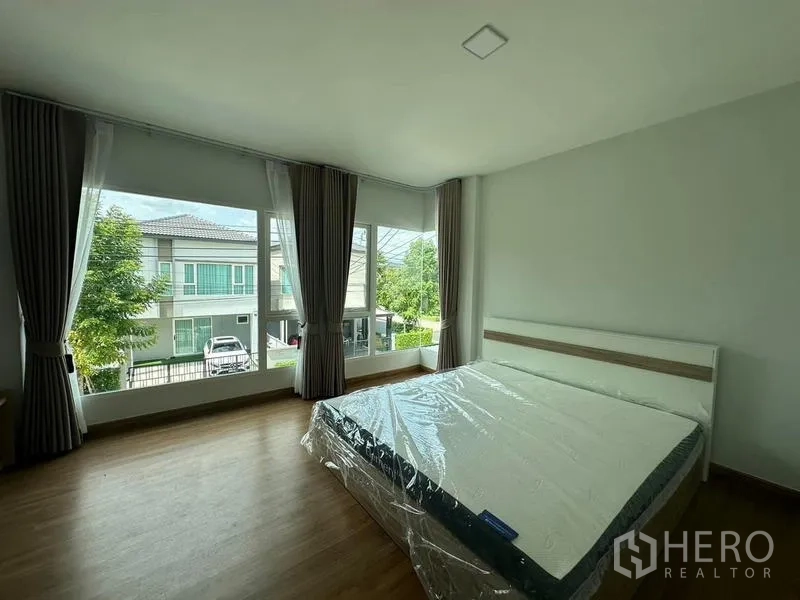 Detached House for rent in Bang Phli, Samut Prakan - Spacious master bedroom with corner windows, wood flooring, and full curtains.