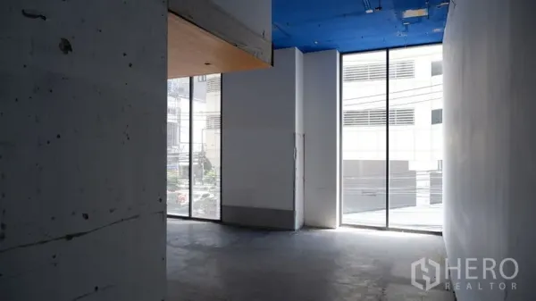 零售空间 出租在Watthana, Bangkok - 空置零售室内，混凝土地面，高挑蓝色天花与落地窗采光充足。