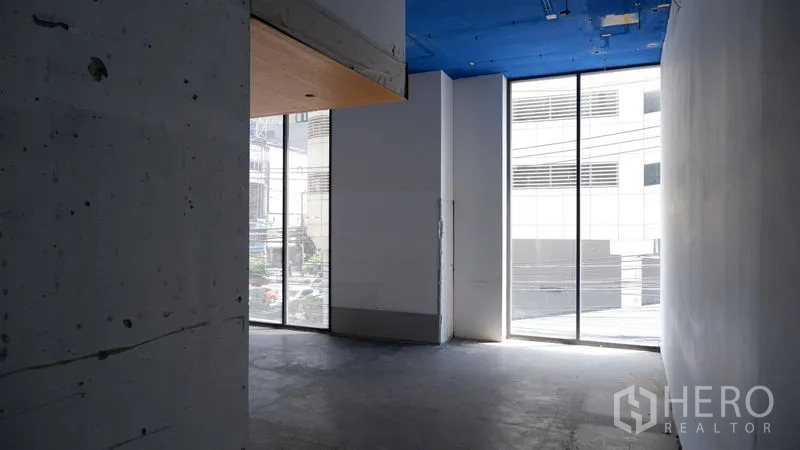 零售空间 出租在Watthana, Bangkok - 空置零售室内，混凝土地面，高挑蓝色天花与落地窗采光充足。