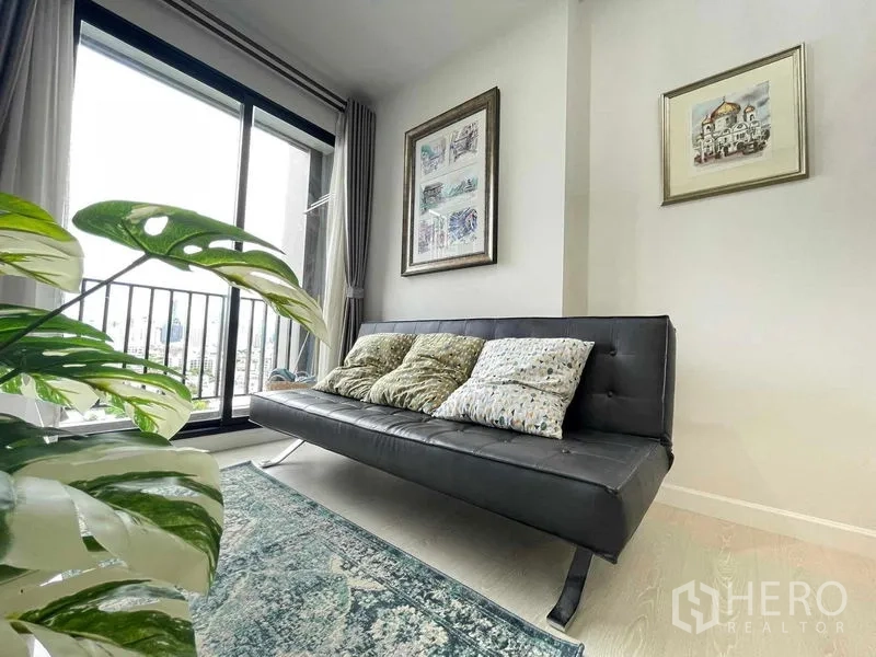 Condominium for sale in Huai Khwang, Bangkok - Living area with black sofa, patterned rug and sliding glass door to the balcony city view.