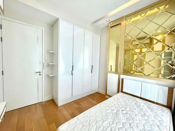 Condominium for rent in Bangkok - Light bedroom with white wardrobe, gold mirrored partition and wood floors.
