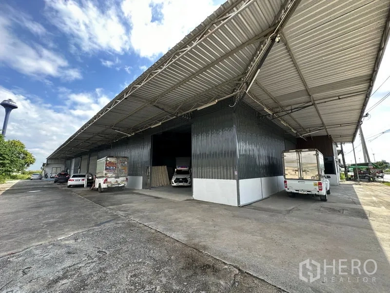 货栈 出租在Khlong Luang, Pathum Thani - 金属外墙大型仓库，带宽阔遮雨装卸区与车道停放车辆。