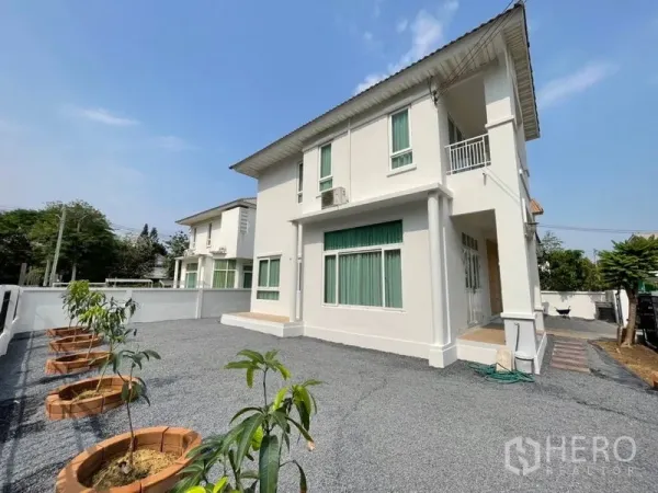 Detached House for sale in Lat Krabang, Bangkok - Side view of the two-storey home with large gravel driveway and a row of young trees in planters.