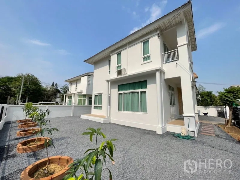Detached House for sale in Lat Krabang, Bangkok - Side view of the two-storey home with large gravel driveway and a row of young trees in planters.