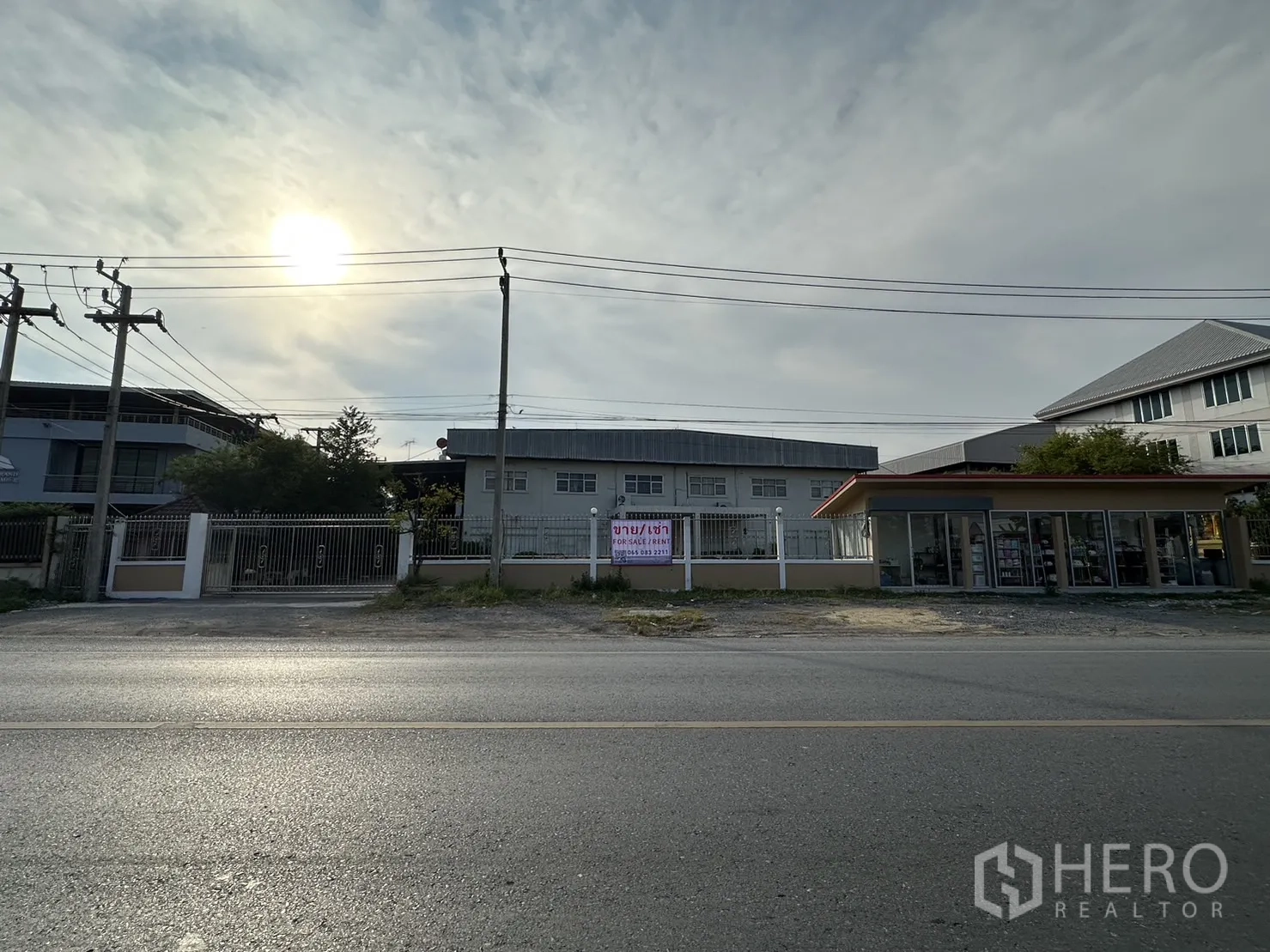 โรงงาน ให้เช่าหรือขายในLam Luk Ka, Pathum Thani - ภาพมุมกว้างริมถนนด้านหน้าโรงงาน มีป้ายขาย/เช่า และอาคารร้านค้าข้างเคียง