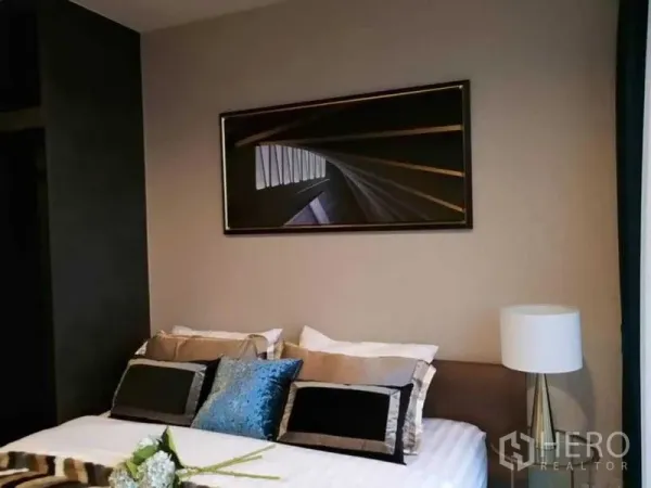 Condominium for rent in Chatuchak, Bangkok - Modern bedroom with upholstered bed, layered pillows, bedside lamp and abstract artwork above the headboard.