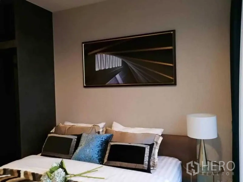 Condominium for rent in Chatuchak, Bangkok - Modern bedroom with upholstered bed, layered pillows, bedside lamp and abstract artwork above the headboard.