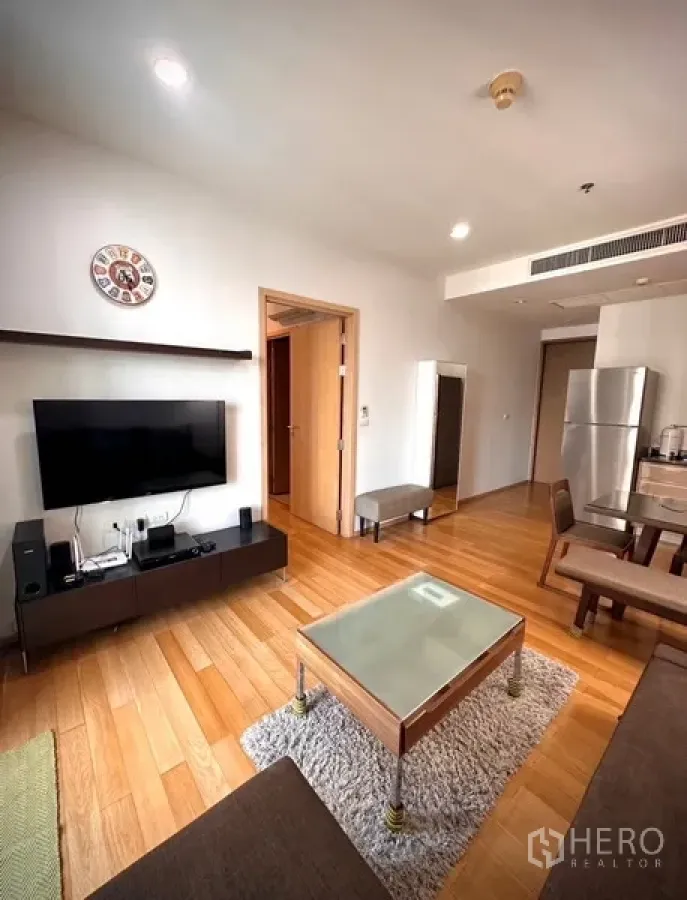 Condominium for rent or sale in Watthana, Bangkok - Bright living room with wood floors, wall-mounted TV, glass coffee table, dining nook and stainless refrigerator.
