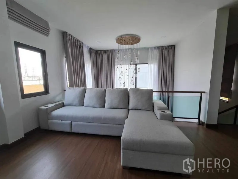 Detached House for rent or sale in Bang Phli, Samut Prakan - Second view of upper living area showing L‑shaped sofa, chandelier and corner windows.