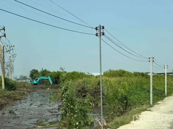 Land for sale in Mueang Samut Sakhon, Samut Sakhon - Excavator clearing vegetation next to a drainage channel and utility lines.