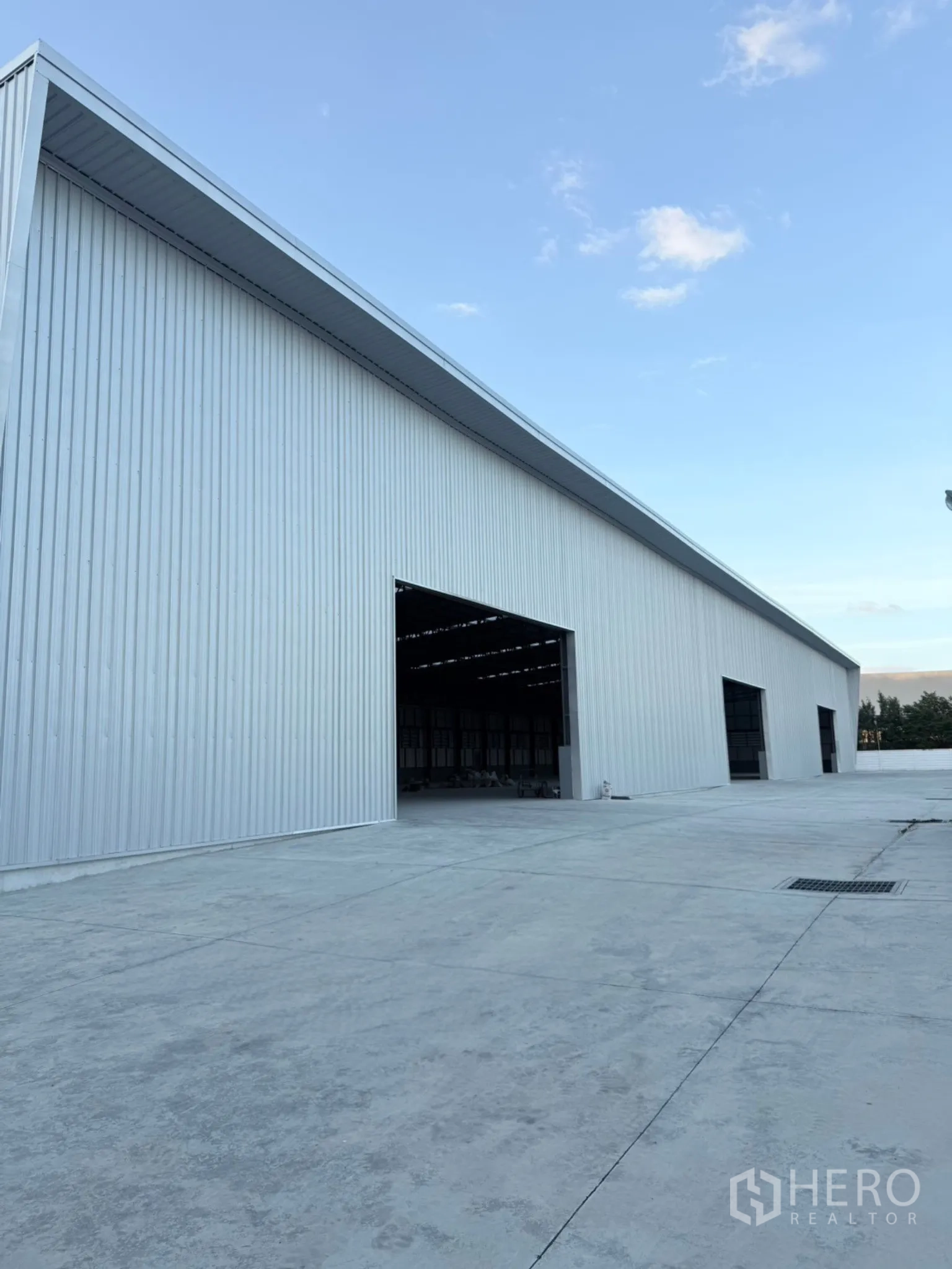 Factory for sale in Ban Bueng, Chon Buri - Long silver warehouse exterior with large open bay doors and wide apron.
