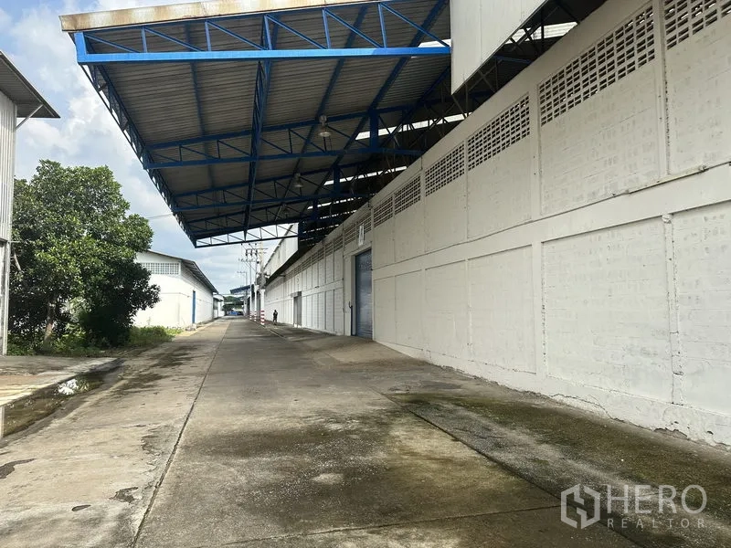 工厂 出租在Nonthaburi - 蓝色钢结构雨棚下的装卸区与长条厂区通道