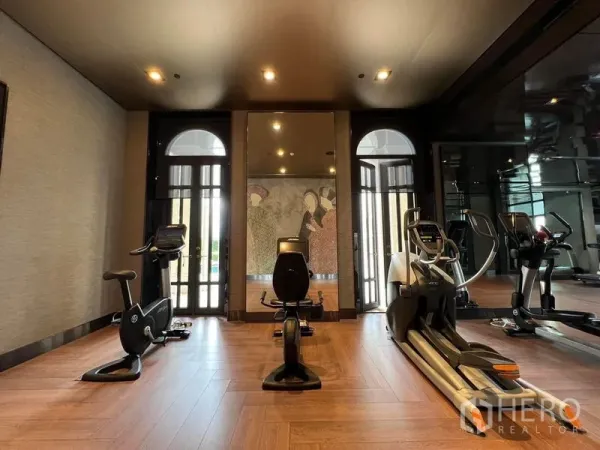 คอนโด ให้เช่าในWatthana, Bangkok - ห้องฟิตเนสของคอนโดพร้อมเครื่องคาร์ดิโอ กระจกบานใหญ่ และพื้นไม้ใกล้หน้าต่างซุ้มโค้งสูง