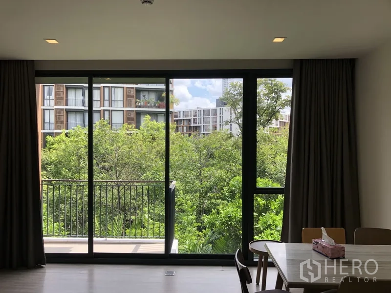 Condominium for rent in Watthana, Bangkok - Floor-to-ceiling sliding doors opening to a balcony with lush greenery and low-rise building views.