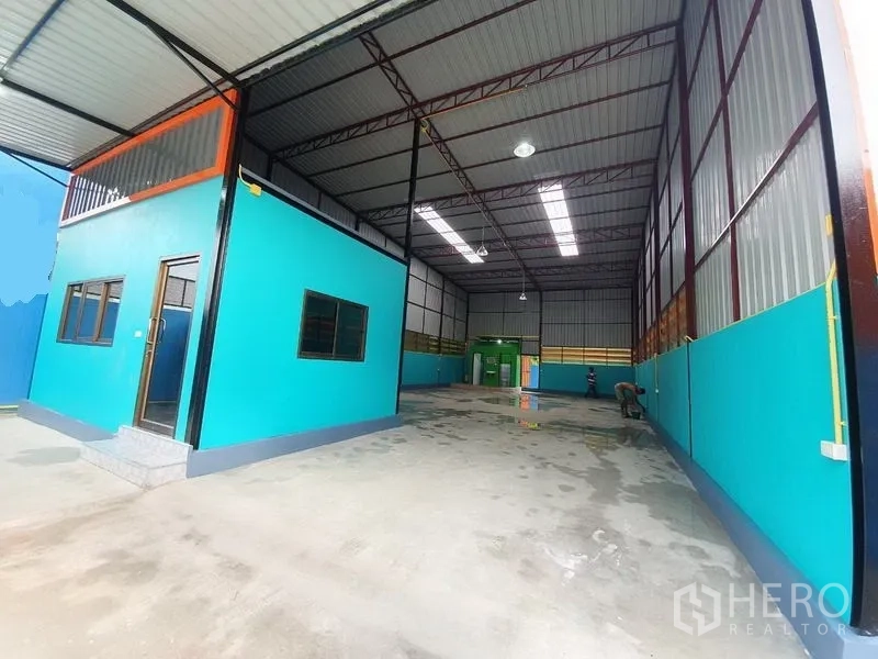 Warehouse for rent in Nonthaburi - Warehouse entry with double-height space, skylight panels and an office structure by the loading area.