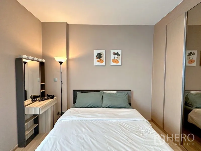Condominium for sale in Watthana, Bangkok - Minimalist bedroom with double bed, wardrobe, dressing table and warm standing lamp.