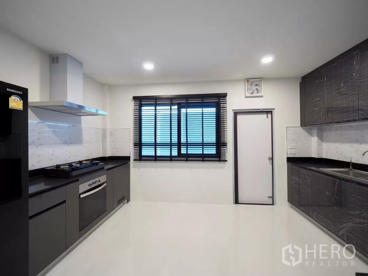 Detached House for rent in Bang Phli, Samut Prakan - Fully fitted Thai kitchen with gas hob, hood, dark countertops and window.