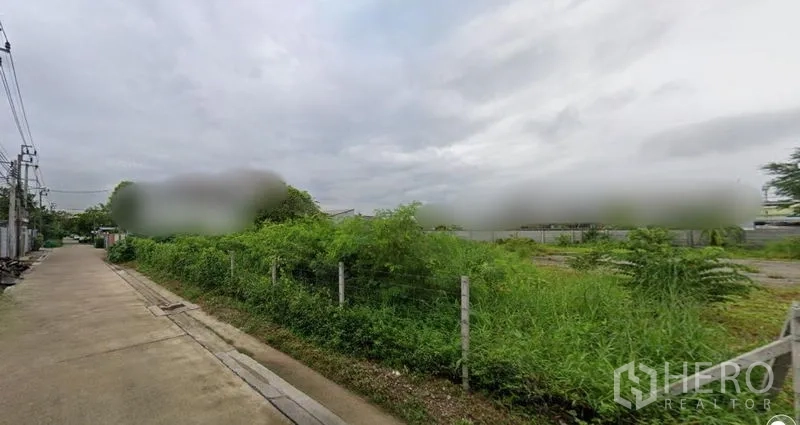 ที่ดิน ให้เช่าในPrawet, Bangkok - มุมมองหัวมุมแปลงที่ดินมีรั้ว ติดถนนคอนกรีต มีสายสาธารณูปโภคและอาคารข้างเคียง เขตประเวศ กรุงเทพฯ