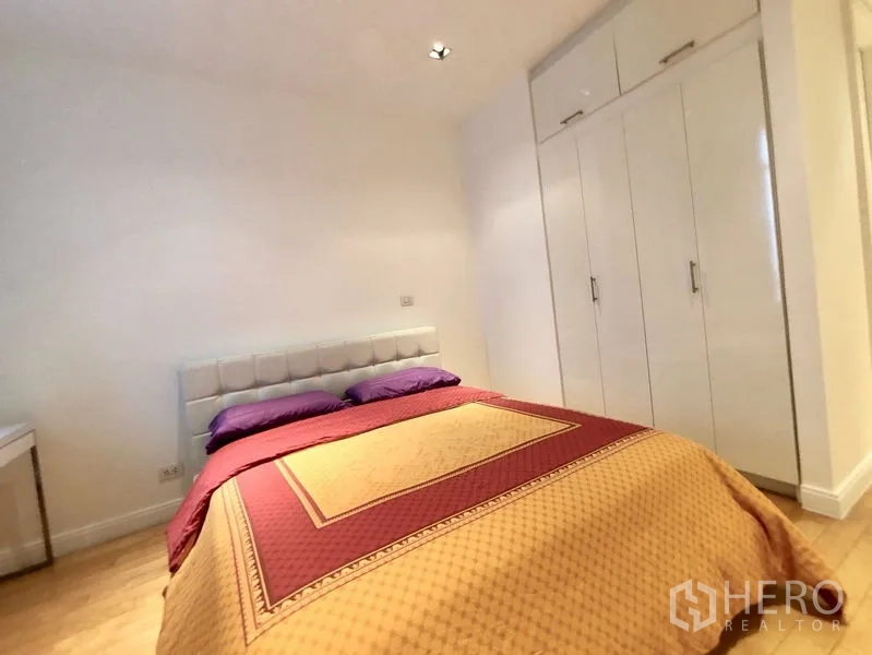 Condominium for rent in Pathum Wan, Bangkok - Second bedroom with bed and glossy white built‑in wardrobes.