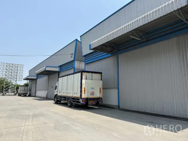 คลังสินค้า ให้เช่าในBang Phli, Samut Prakan - อาคารโกดังผนังเมทัลชีทพร้อมชายคาโหลดสินค้าและรถบรรทุกในลานคอนกรีตกว้าง