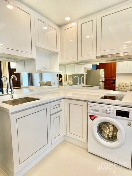 Condominium for sale in Huai Khwang, Bangkok - U-shaped white kitchen with stone countertop, sink, hob and front-load washer.