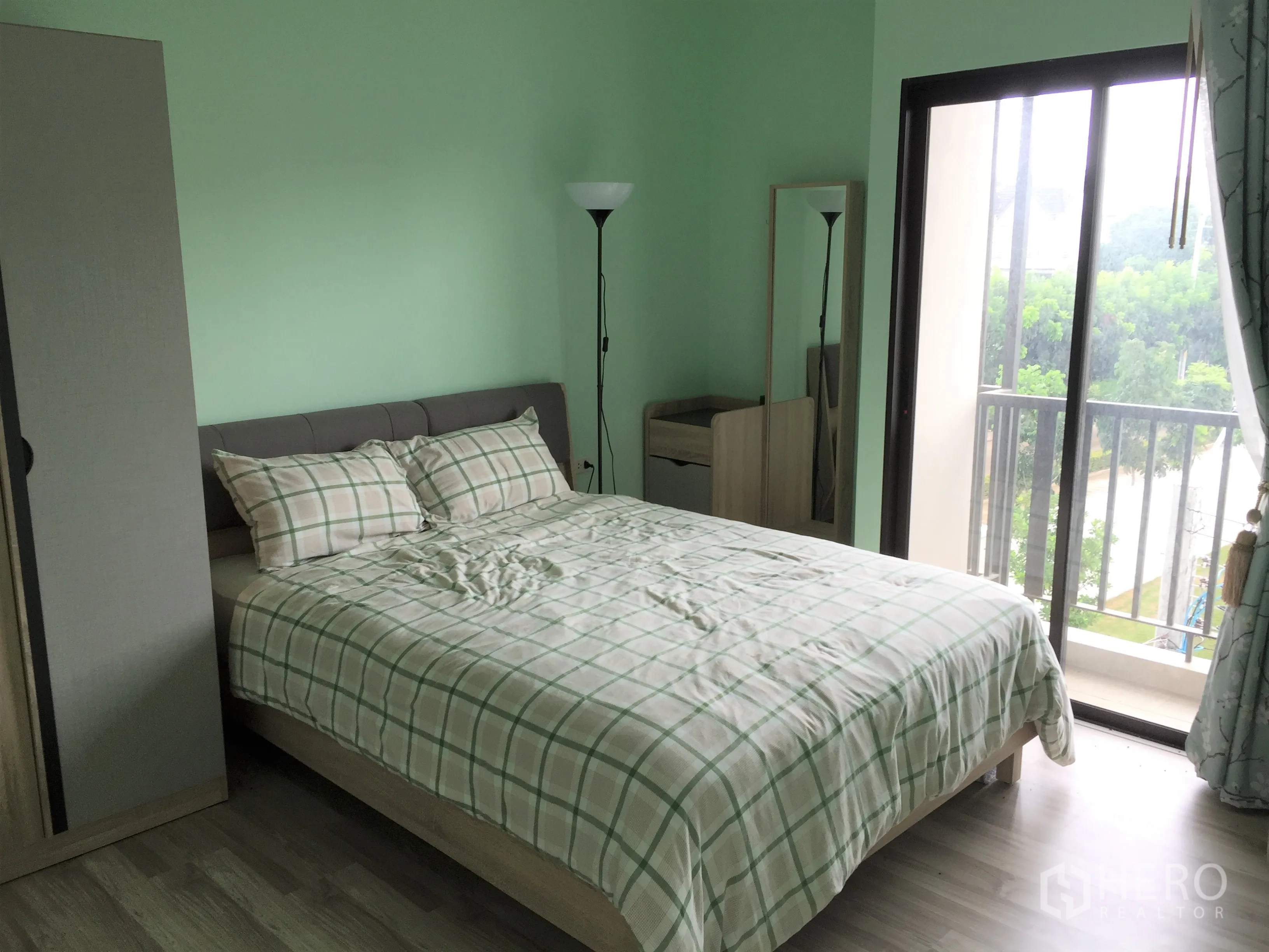 Townhouse for rent in Saphan Sung, Bangkok - Secondary bedroom with mint walls, wardrobe and sliding door to a small balcony with trees.
