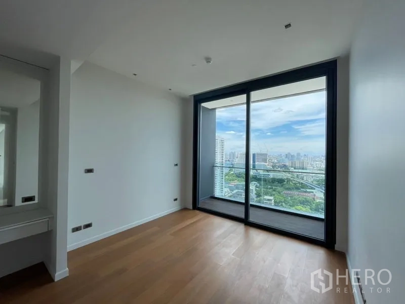 Condominium for rent or sale in Bangkok - Bright bedroom with wood floors and large sliding glass doors opening to a balcony with panoramic city views.