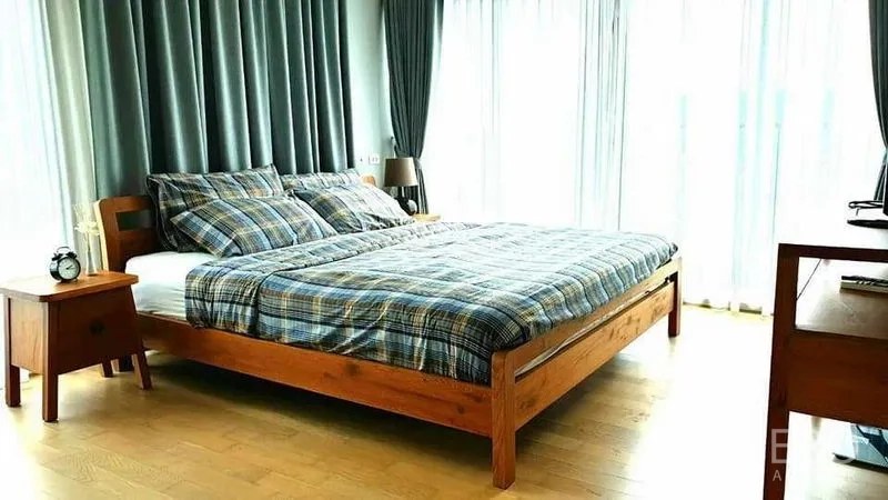 Condominium for rent or sale in Watthana, Bangkok - Sunlit master bedroom with wooden bed, plaid bedding and floor‑to‑ceiling curtains.