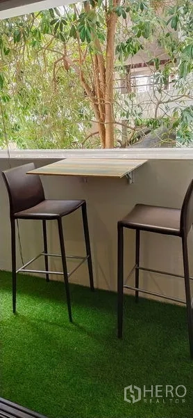 公寓 出售在Watthana, Bangkok - 人造草坪阳台，折叠墙桌与两把高脚椅，绿树景观。