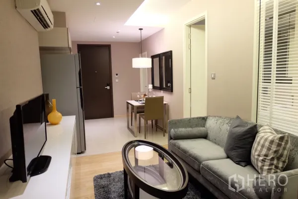 Condominium for rent in Watthana, Bangkok - Bright living room with gray sofa, oval glass coffee table, TV console and a dining nook under soft pendant lighting.