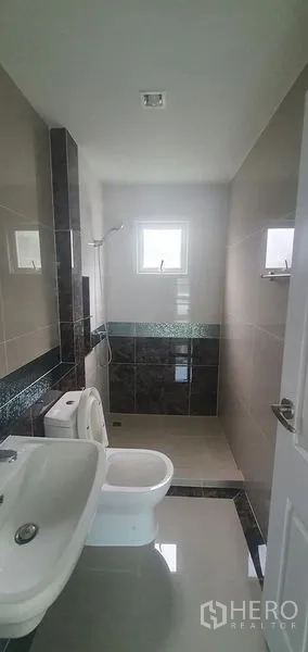 Detached House for rent in Nonthaburi - Bright tiled bathroom with window, shower zone, sink and toilet in a detached house in Pak Kret, Nonthaburi.