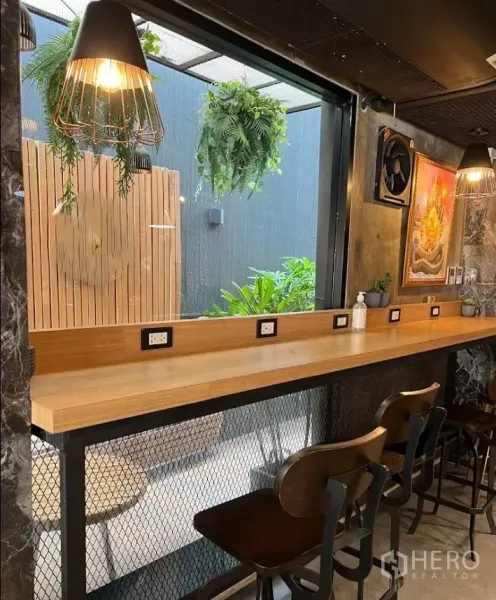พื้นที่ขายปลีก ให้เช่าในKhlong Toei, Bangkok - มุมมองด้านข้างของเคาน์เตอร์สูงพร้อมโคมแขวน เฟิร์นห้อย และเก้าอี้สูงข้างผนังตกแต่ง