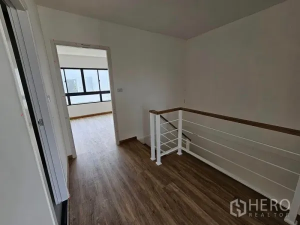 联排别墅 出租在Bang Kapi, Bangkok - 二层过道，木纹地板与白色栏杆楼梯，连通采光充足的卧室与大窗。