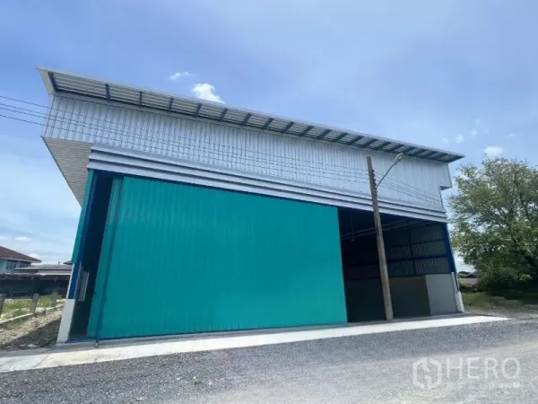 Warehouse for rent in Min Buri, Bangkok - Side elevation of the warehouse with closed teal panels and a streetlight in front.