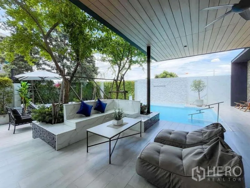 Detached House for sale in Bang Lamung, Chon Buri - Shaded terrace with built‑in seating, coffee table and beanbags overlooking the pool.