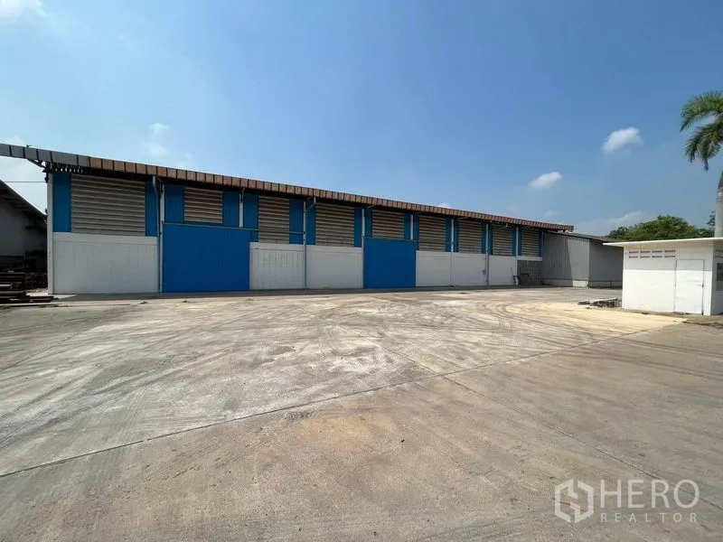 货栈 出租在Bang Pa-in, Phra Nakhon Si Ayutthaya - 仓库外立面，蓝色推拉门与宽阔混凝土场地便于卡车掉头