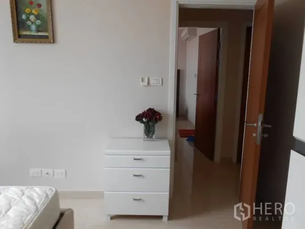 คอนโด ให้เช่าในWatthana, Bangkok - มุมห้องนอนพร้อมตู้ลิ้นชักสีขาว ภาพแขวนผนัง และประตูไม้เปิดสู่โถงทางเดิน