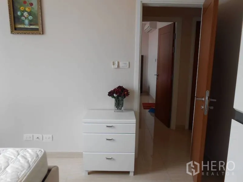 คอนโด ให้เช่าในWatthana, Bangkok - มุมห้องนอนพร้อมตู้ลิ้นชักสีขาว ภาพแขวนผนัง และประตูไม้เปิดสู่โถงทางเดิน