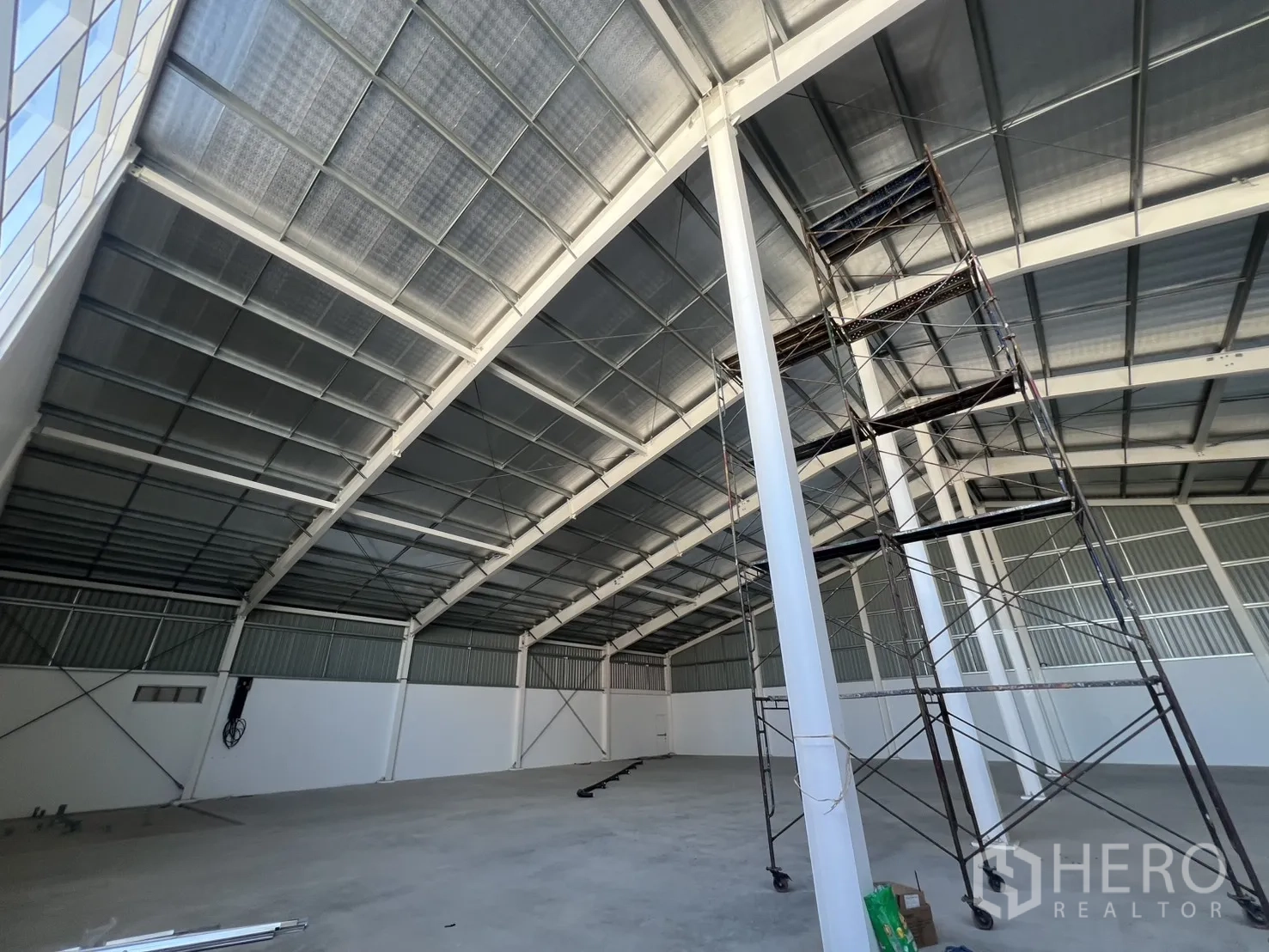 Warehouse for rent in Min Buri, Bangkok - High-ceiling warehouse showing steel rafters and mobile scaffolding for maintenance.