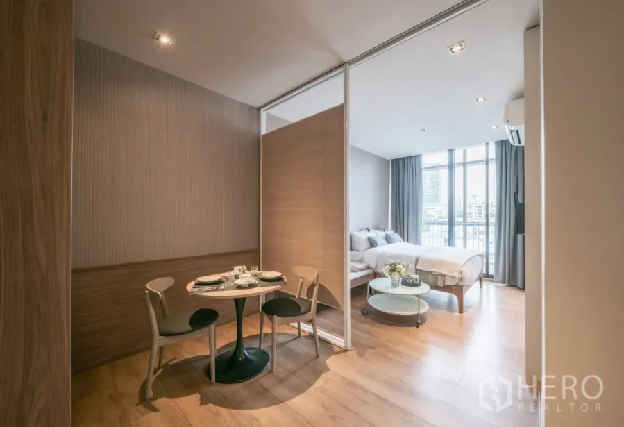 Condominium for rent in Khlong Toei, Bangkok - Open-plan studio condo with sliding partition, dining table and floor-to-ceiling windows.